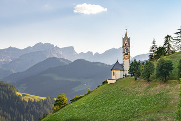 Church on a steep hillside with mountain peaks in the background in La Valle, South Tyrol, Italy	