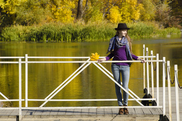 Girl in hat standing on the dock. Autumn, sunny.