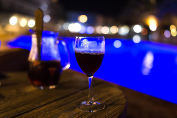 Glass of sangria on the wooden table at night by the pool
