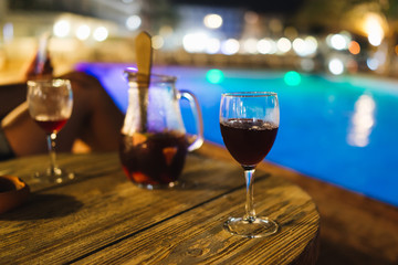 Glass of sangria on the wooden table at night by the pool
