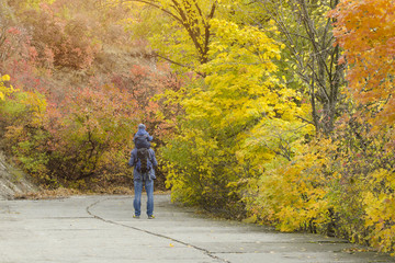 Father and son on their shoulders walk through the autumn park. Back view