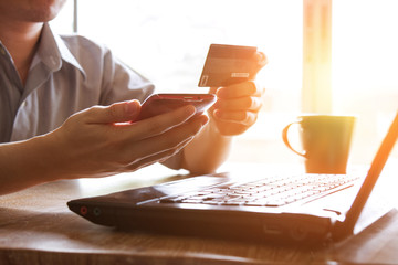 man holding credit card and using mobile phone and laptop computer