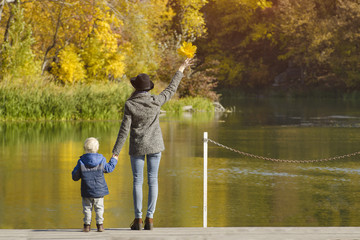 Fototapeta na wymiar Mom and son are standing on the pier by the river. Autumn, sunny. Back view
