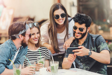 Happy friends looking something in the smartphone and enjoying time together at the summer cafe