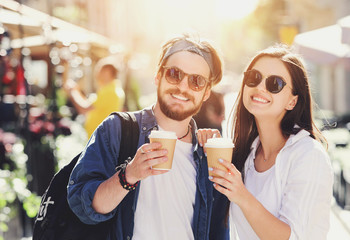 Two attractive best friends in sunglasses walking outdoors at the sunny summer street and drinking cofee