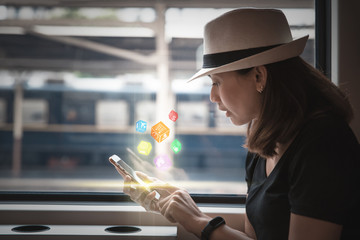 Beautiful young woman traveler using smartphone with icon digital box social network at a train station , Transportation and travel lifestyle concept
