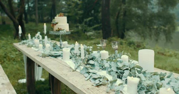 Lovely decorations for romantic date in foggy wood: candles, leaves, flowers and beautiful two-tiered cake with berries. 4k.