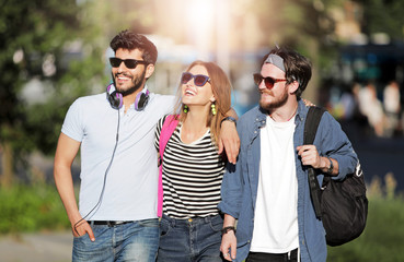 Three attractive multicultural friends walking outdoors at the sunny day and smiling