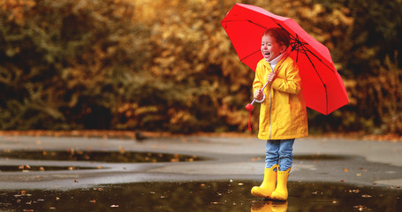 Obraz premium happy child girl with an umbrella and rubber boots in puddle on autumn walk