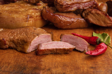 Sliced smoked meat and lard with meat veins on a wooden background with red pepper