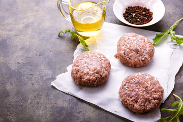 Raw ground meat patties on a paper and mettal rustic table. Fresh beef and pork mince, vegetable oil, spices, arugula