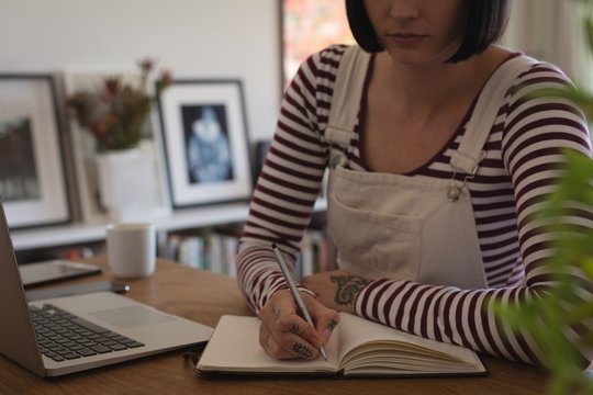 Mid section of woman writing on diary at home