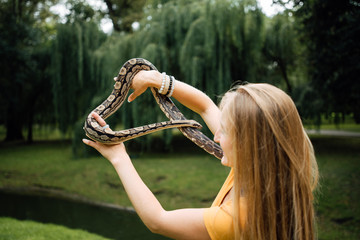 beautiful blonde girl is holding a snake in her hands. Contact the zoo.