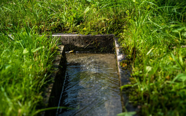 Wooden gutter for water supply. Decorative system of garden watering