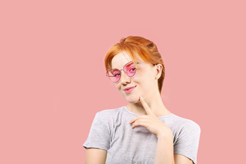 Attractive young woman with long red hair, wearing pink cat eye sunglasses, showing flirtatious body language, touching face. Beautiful redhead female flirty facial expression. Background, copy space.