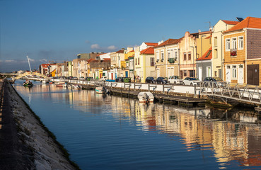 Fototapeta na wymiar Canal de São Roque in the city of Aveiro, Portugal, flanked by colorful houses, boats anchored and in the background a moliceiro to pass under the bridge of Carcavelos.