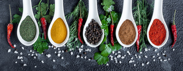 assortment of indian spices and herbs in ceramic spoon on black background, chili peppers and...