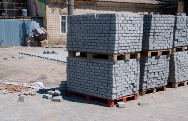 Pavement repair on the street outdoors. Wooden palettes loaded with gray cobblestone lyng on one...
