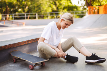 Young skater girl holding her painful leg with skateboard near at skatepark
