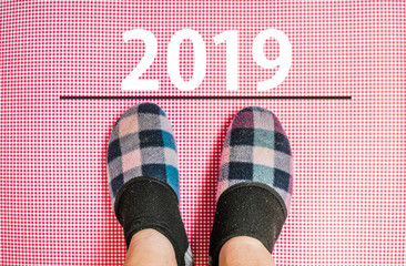 happy new year 2019. legs in slippers standing next to line and number 2019