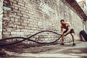 Athletic man working out with rope in front of brick wall. Strength and motivation. Outdoor workout.