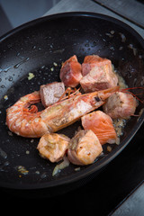 pieces of salmon and shrimp are fried in oil in a frying pan