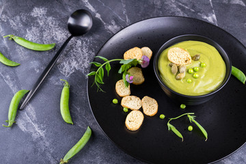 Green pea soup puree with croutons in black bowl.  On dark stone background
