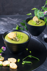Bowl of  homemade green spring pea soup topped with pumpkin seeds,  croutons. On dark stone background