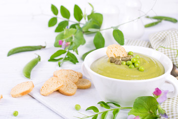 Green pea soup puree with croutons in black bowl.  On white background