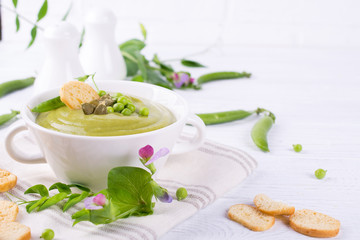 Light summer  delicious green peas cream soup served with pumpkin seeds,  croutons on white background.