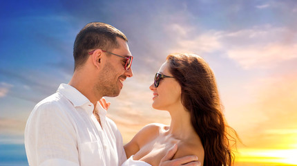 love, summer and relationships concept - happy smiling couple in sunglasses hugging over evening sky background