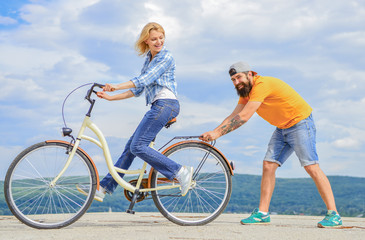 Teach adult to ride bike. Man helps keep balance and ride bike. Find balance. Woman rides bicycle sky background. How to learn to ride bike as an adult. Girl cycling while boyfriend support her