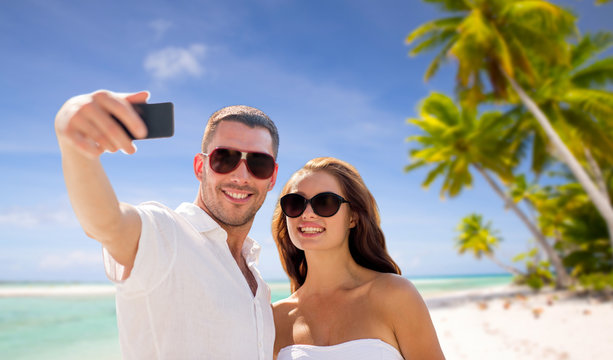 travel, tourism and summer vacation concept - smiling couple in sunglasses making selfie by smartphone over tropical beach background in french polynesia