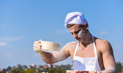 Man muscular baker or cook sifts flour through sieve. Hands of chef cook covered with sticky dough and flour. Baker at working with flour and sieve, kneading dough. Pizzaiolo concept