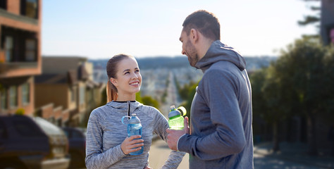 fitness, sport and people concept - smiling couple with bottles of water over golden gate bridge in san francisco bay background