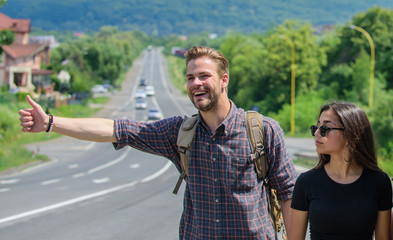 Couple travelers man and girl hitchhiking at edge road nature background. Travel by autostop. Couple hitchhikers travelling summer sunny day. Hitchhiking is one of cheapest ways of traveling