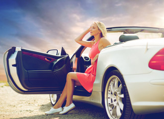 travel, road trip and people concept - happy young woman posing in convertible car over evening sky background