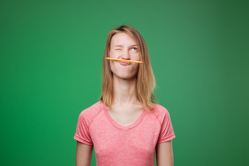 Funny student in pink t-shirt playing holding pen between nose and lips as mustache.