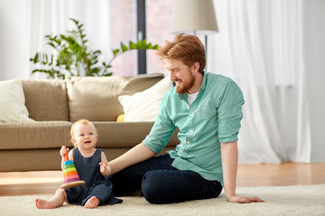 family, fatherhood and people concept - happy red haired father with ball playing with little baby daughter at home