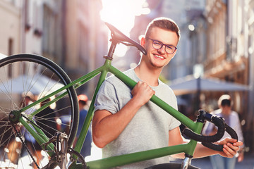 Young hipster light-hair boy in glasses holding green bicycle at sunny summer street