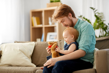 family, fatherhood and people concept - happy red haired father and little baby daughter playing with teddy bear at home
