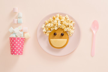 Baby pancakes for breakfast. Creative idea for the kid dessert: delicious pancakes in the form of the happy face with the hair making popcorn