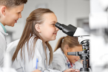education, science and children concept - kids or students with microscope studying biology at...