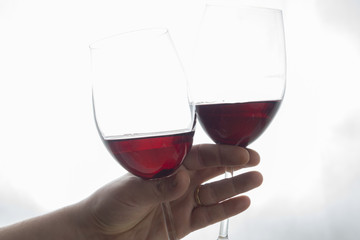 hand holding two wineglasses with red wine