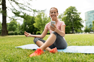 Fototapeta premium fitness, sport and technology concept - woman with smartphone and earphones resting on exercise mat at park