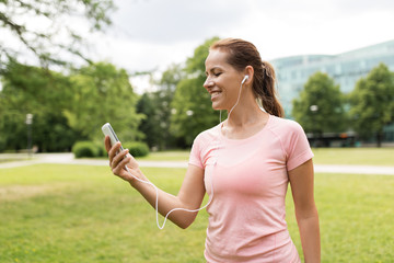 fitness, sport and healthy lifestyle concept - smiling woman listening to music on smartphone at park