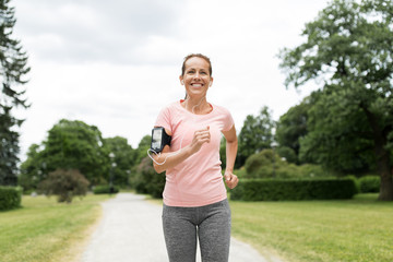 fitness, sport and healthy lifestyle concept - smiling woman with earphones wearing armband with...