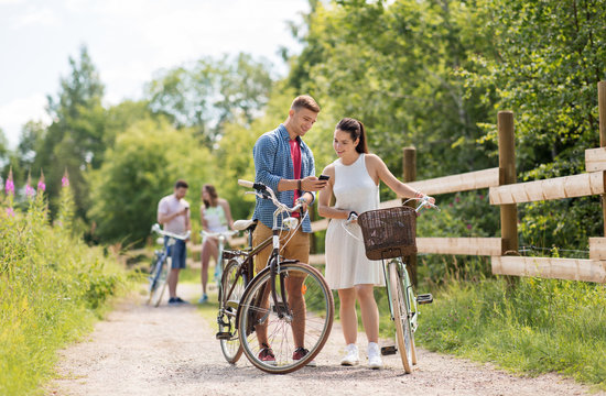 people, technology and lifestyle concept - happy couple with bicycles and smartphone at country in summer