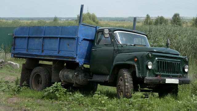 The old car is a truck. It stands in a village on the roadside with a blue body.