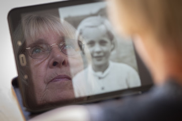 Senior caucasian woman looking at old photos of herself as a young woman on a tablet computer...